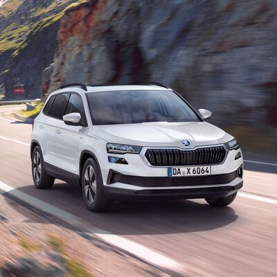 Ein weißer Škoda Karoq fährt dynamisch eine kurvige Bergstraße entlang, präsentiert von Škoda Auto Röhr.