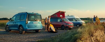 Drei Freizeitfahrzeuge parken in einer ländlichen Landschaft, während Menschen sich auf Outdoor-Aktivitäten vorbereiten.