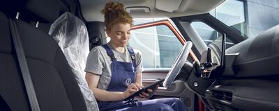 Eine Mechanikerin im Blaumann arbeitet mit einem Tablet im Innenraum eines Autos bei Auto Röhr.