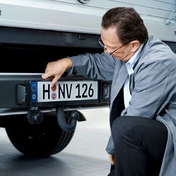 Ein Mechaniker überprüft das Nummernschild während einer Haupt- und Abgasuntersuchung bei Auto Röhr.