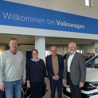 Vier Personen stehen lächelnd vor einem "Willkommen bei Volkswagen"-Schild im Auto Röhr Showroom.