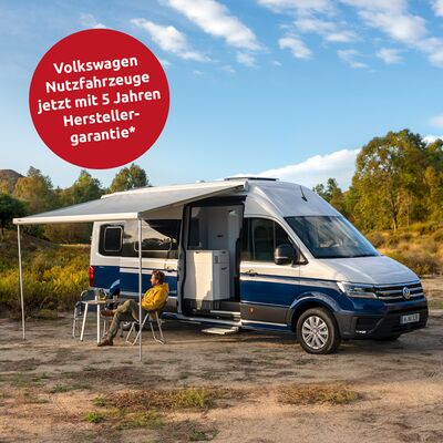 Ein Campervan von Volkswagen mit ausgefahrener Markise steht in einer malerischen Landschaft. Ein Mann sitzt entspannt davor.