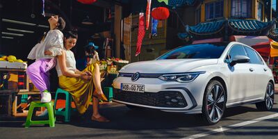 Ein weißer Volkswagen Golf GTE steht vor einem Marktstand mit zwei Frauen. | Škoda Auto Röhr.