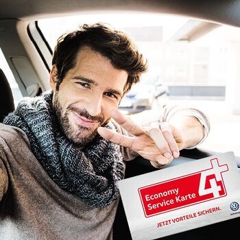 Ein Mann sitzt lächelnd im Auto und hält eine Economy Service Karte hoch