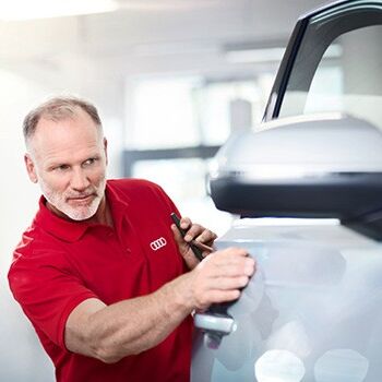 Ein Techniker im roten Polohemd führt einen Lackservice an einem Auto durch.
