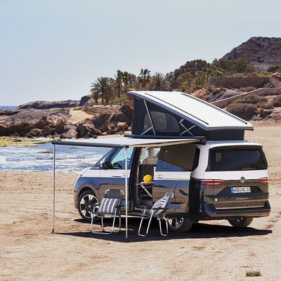 Ein Campervan mit ausgeklapptem Dach und Markise steht am Strand. Zwei Stühle sind aufgestellt. | Auto Röhr