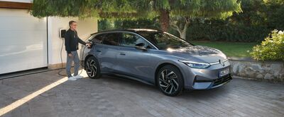 Ein Mann lädt ein modernes Elektroauto vor einer Garage auf. Im Hintergrund sind Bäume und ein gepflegter Garten zu sehen. Volkswagen Zentrum Passau.