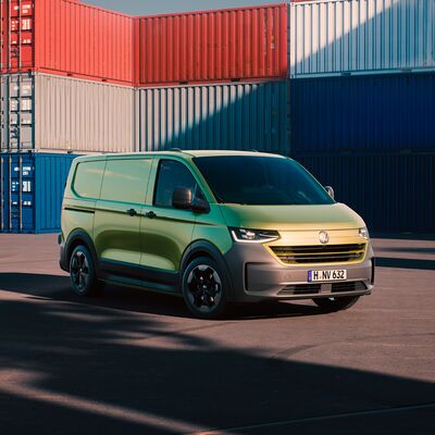 Grüner Volkswagen Transporter vor bunten Containern auf einem Parkplatz. Volkswagen Zentrum Passau.