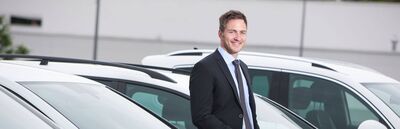 Ein lächelnder Mann im Anzug steht vor mehreren weißen Autos beim Volkswagen Zentrum Passau.
