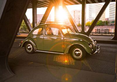 Ein klassischer VW Käfer fährt bei Sonnenuntergang unter einer Brücke, inspiriert von Auto Röhr.