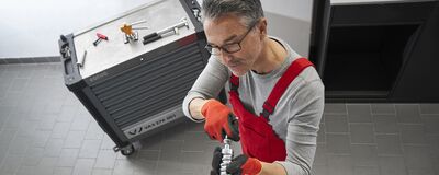 Ein Mechaniker in roter Latzhose arbeitet an einem Werkzeug in einer Werkstatt von Škoda Auto Röhr.