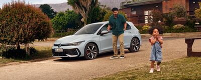 Ein Mann und ein Kind spielen fröhlich vor einem modernen Volkswagen R-Line auf einem sonnigen Platz.