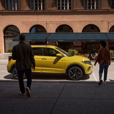 Zwei Personen nähern sich einem gelben VW T-Cross vor einem Café. | Škoda Auto Röhr.