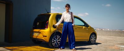 Eine Frau steht neben einem gelben Elektroauto und lädt es auf, das bei Auto Röhr erhältlich ist.