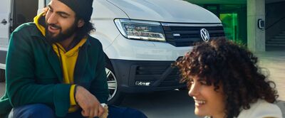 Zwei lächelnde Personen sitzen vor einem weißen Volkswagen Transporter. | Volkswagen Zentrum Passau