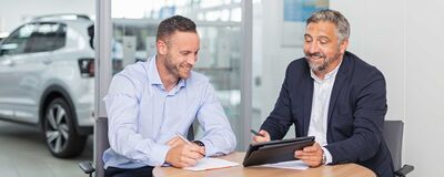Zwei Männer besprechen fröhlich ein Dokument an einem Tisch im Auto Röhr Showroom.