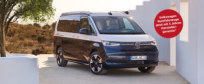 Ein Volkswagen-Bus steht vor einem modernen Gebäude in sonniger Landschaft. Text wirbt für 5 Jahre Garantie. Volkswagen Zentrum Passau.