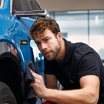 Ein Mitarbeiter poliert sorgsam ein blaues Auto.