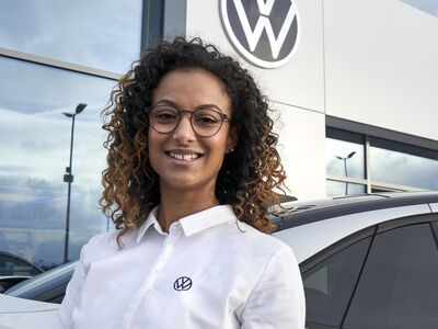 Frau in weißem Hemd vor einem Volkswagen-Zentrum in Passau, neben einem Auto.