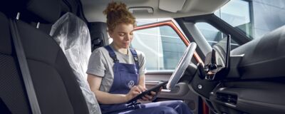 Eine Mechanikerin im Blaumann arbeitet mit einem Tablet im Innenraum eines Autos bei Auto Röhr.