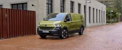 Grüner Volkswagen-Transporter auf gepflasterter Straße neben modernem Gebäude. Ideal für Auto Röhr.