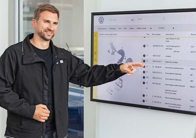 Ein Mann zeigt auf einen Bildschirm mit Autoteilen, was auf die Expertise von Auto Röhr in der Teileverwaltung hinweist.
