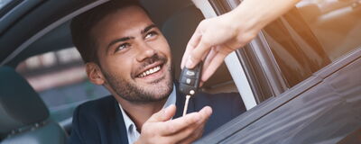 Mann im Auto erhält Autoschlüssel, lächelnd und zufrieden. Perfekt für Škoda Auto Röhr.