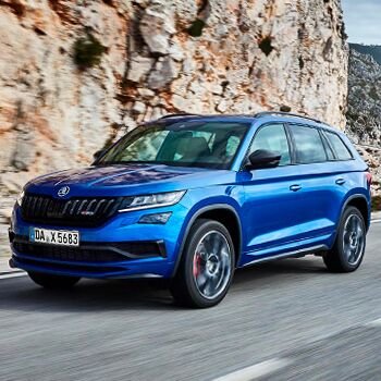 Ein blauer Škoda Kodiaq fährt dynamisch entlang einer kurvigen Straße, präsentiert von Auto Röhr.