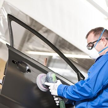 Ein Techniker poliert konzentriert eine Autotür in der Werkstatt.