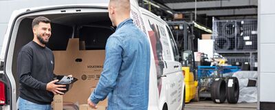 Zwei Männer laden in einem Lagerraum Kartons in einen Transporter mit der Aufschrift Volkswagen Zentrum Passau.