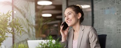 Frau im Büro telefoniert lächelnd, umgeben von Pflanzen, mit Fokus auf Serviceassistenz. | Škoda Auto Röhr.