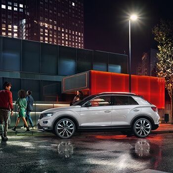 Ein weißer SUV parkt nachts vor einem beleuchteten Gebäude