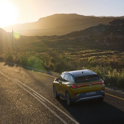 Volkswagen ID.4 fährt bei Sonnenuntergang auf einer malerischen Landstraße. | © IC0075