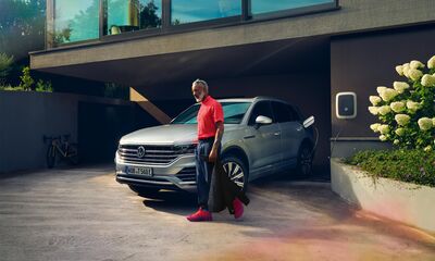 Mann in rotem Hemd steht neben einem silbernen Volkswagen Touareg vor einem modernen Haus. | Škoda Auto Röhr.
