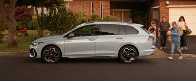 Ein silberner Kombi parkt vor einem Backsteinhaus, während eine Familie vorbeigeht. | Škoda Auto Röhr.