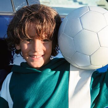 Ein lächelnder Junge in einem Sporttrikot hält einen Fußball vor einem Auto. | Auto Röhr.