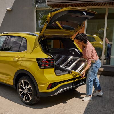 Frau lädt eine Leiter in den Kofferraum eines gelben VW T-Cross beim Auto Röhr ein.