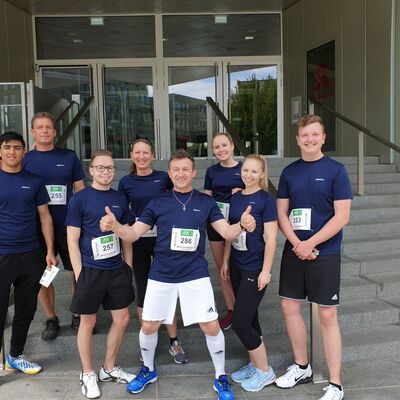 Eine Gruppe von Läufern in blauen Trikots posiert fröhlich vor einem Gebäude, bereit für den Firmenlauf von Auto Röhr.