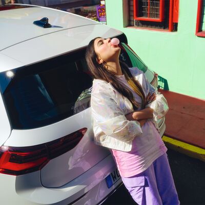 Frau lehnt lässig an einem weißen Auto und bläst Kaugummiblasen. Škoda Auto Röhr.