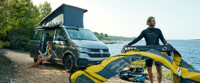 Ein Paar bereitet sich am Strand neben einem Volkswagen-Bus auf das Kitesurfen vor. | Škoda Auto Röhr.