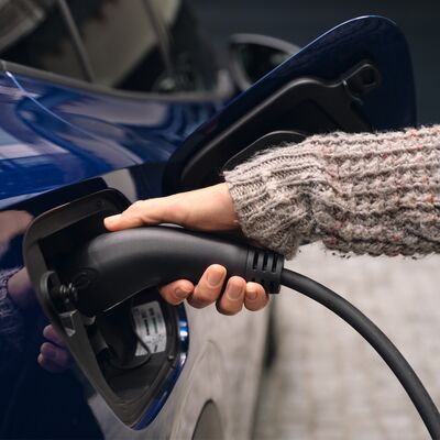 Eine Person lädt ein blaues Elektroauto mit einem Ladekabel auf. | Škoda Auto Röhr