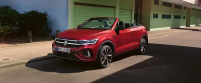 Ein rotes Cabriolet von Volkswagen steht bei sonnigem Wetter vor einer Garage, repräsentativ für Auto Röhr.