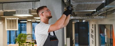 Ein Techniker von Erich Röhr GmbH arbeitet konzentriert an der Installation von Haustechnik in einem modernen Büro.