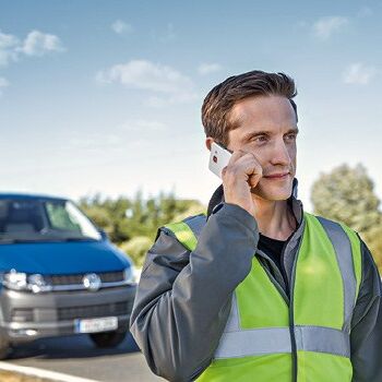 Ein Mann in Warnweste telefoniert vor einem blauen Lieferwagen.