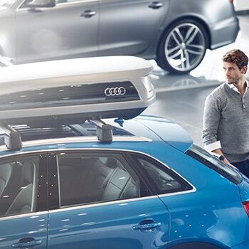 Ein Mann steht neben einem blauen Audi mit Dachbox im Volkswagen Zentrum Passau.