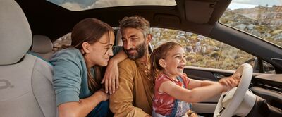 Familie im Auto, lachend und fröhlich. Das Kind hält das Lenkrad. Landschaft im Hintergrund. Škoda Auto Röhr.