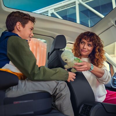 Eine Frau gibt einem Jungen ein Stofftier in einem Auto. Perfekt für Reisen mit Auto Röhr.