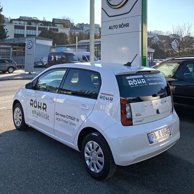 Ein weißer Škoda CITIGOe iV mit Auto Röhr Werbung steht auf einem Parkplatz.