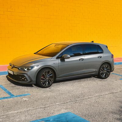Grauer Volkswagen Golf parkt vor einer leuchtend gelben Wand auf einem Parkplatz. | Škoda Auto Röhr.