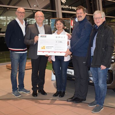 Eine Gruppe von fünf Personen übergibt einen Scheck bei Auto Röhr vor einem Volkswagen Touareg.